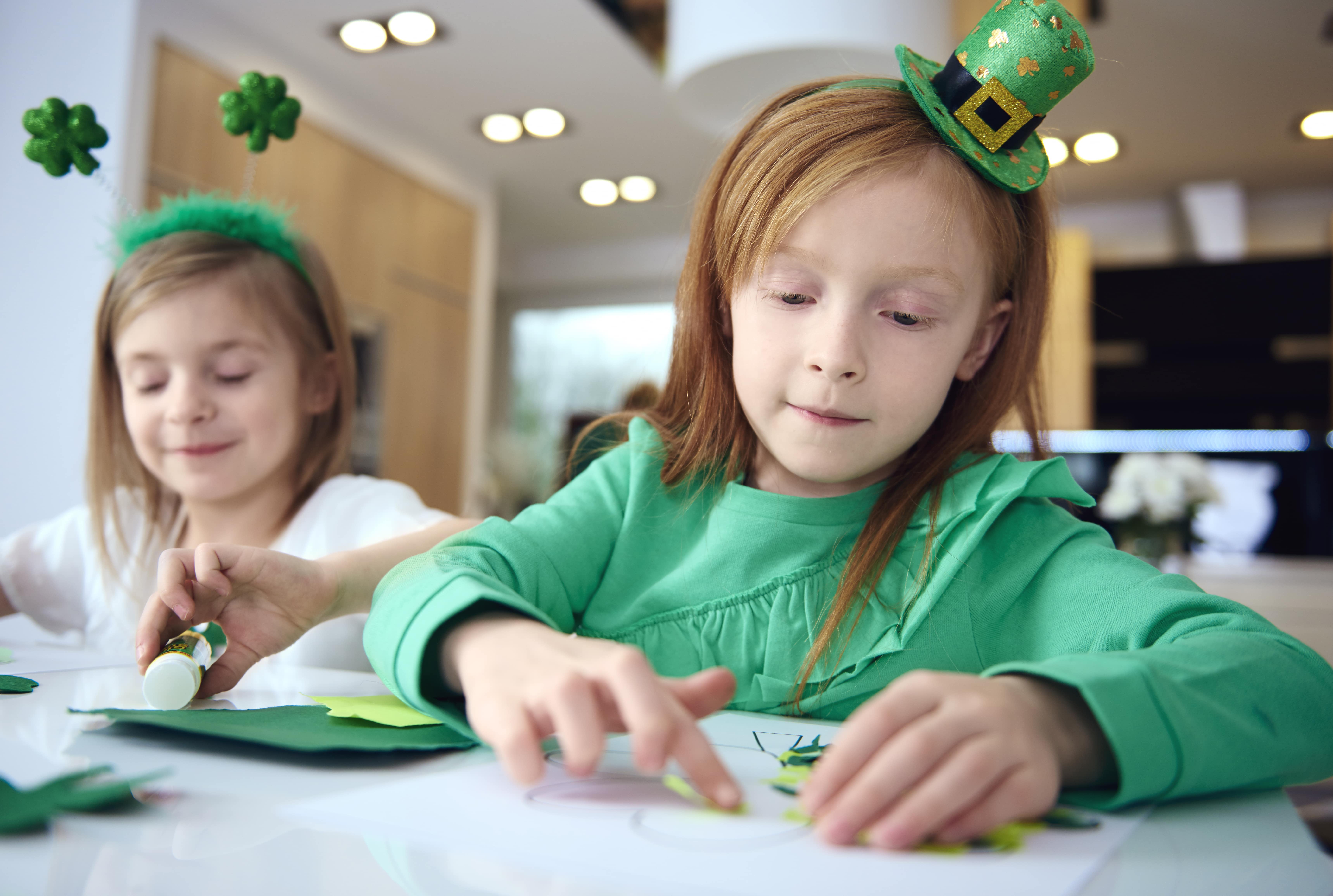 Children sitting at a table dressed in St. Patrick's Day gear making St. Patrick's Day crafts and DIY decor for kids.